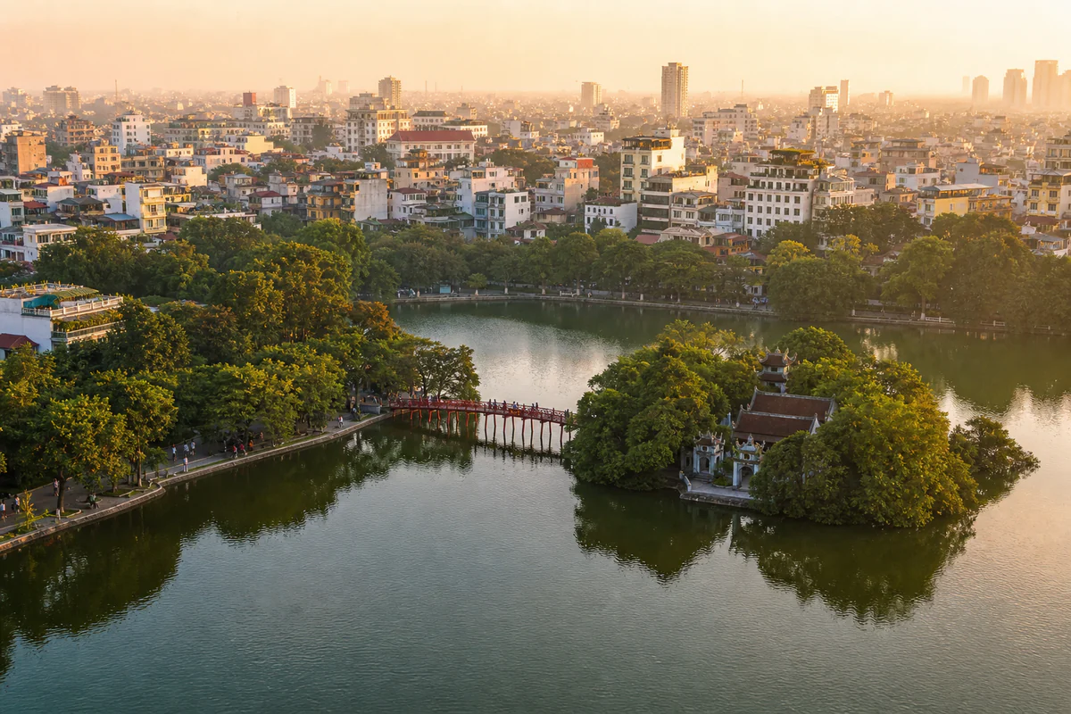 Sunrise aerial view over Hanoi's Hoan Kiem Lake, Old Quarter rooftops, and green cityscape in Vietnam.